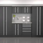 A sleek, modern garage storage unit with a gray finish and white handles. It includes tall cabinets on either side, upper and lower cabinets, drawers, and a countertop workspace. Tools and small containers are organized and displayed above the countertop.